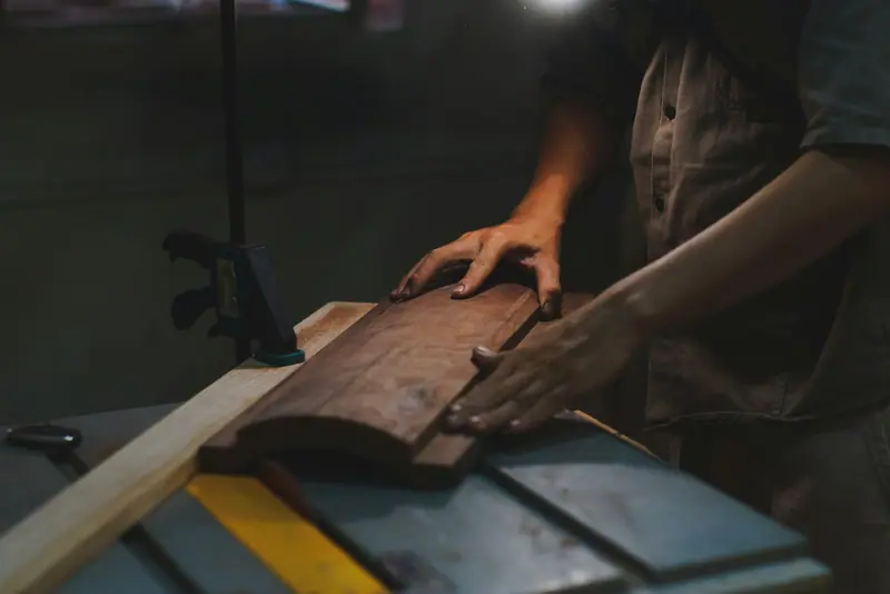 Handen geleiden een houten werkstuk over een zaagmachine